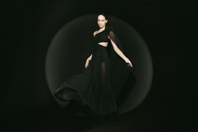 Woman in elegant black dress posing in a photo studio with soft lighting on a black background. Fashion editorial photography.