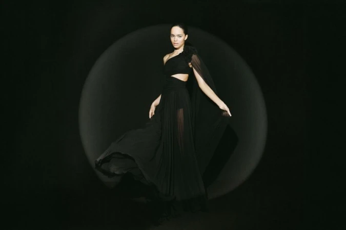Woman in elegant black dress posing in a photo studio with soft lighting on a black background. Fashion editorial photography. 
