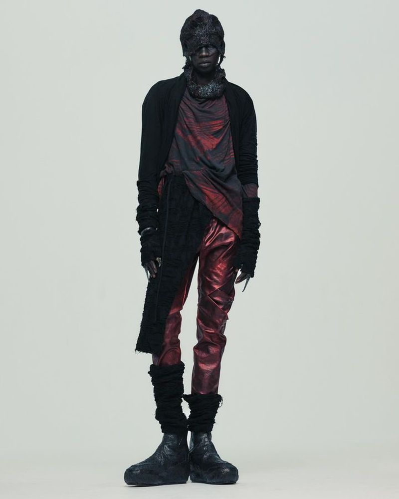 Editorial fashion shot of a singular, androgynous adult model posing in an avant-garde outfit against a neutral background.