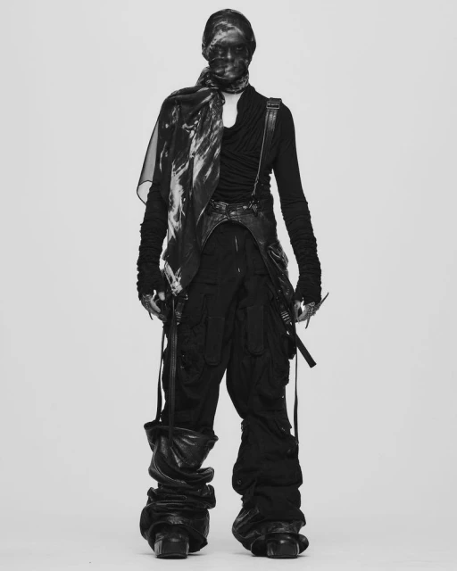 Full-length studio shot of an adult figure wearing a black avant-garde fashion ensemble with scarf covering the face, against a neutral background.