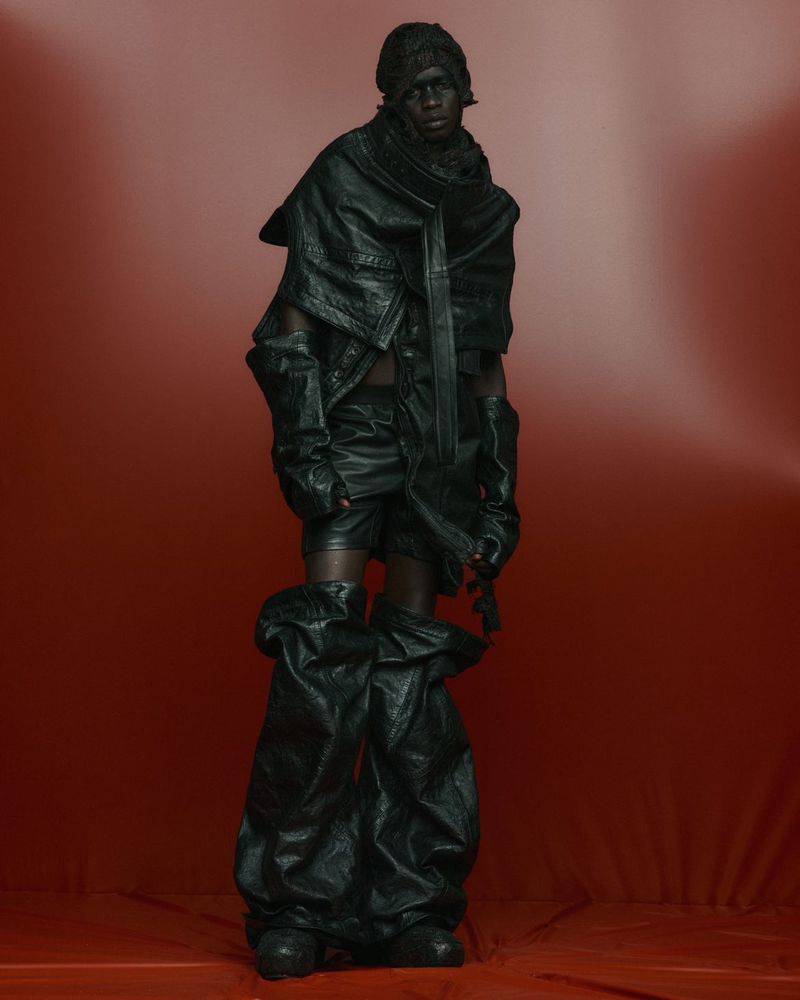 Monochromatic fashion portrait of a person in black leather-like ensemble against a gradient red backdrop, showcasing texture and unique style.