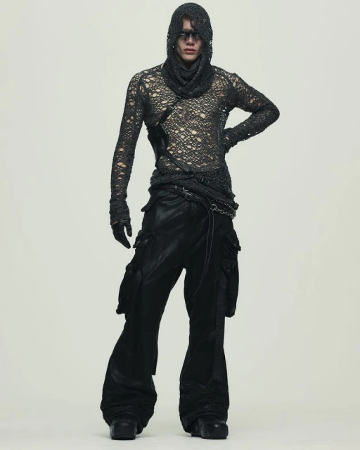 Fashion model poses in a distressed long-sleeve top, cowl, and wide-leg cargo pants in a studio. Full-length shot with neutral background.