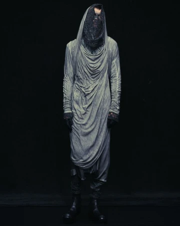 Full-length studio portrait of a person wearing a draped grey robe with a dark mesh covering their head and face, against a black background.