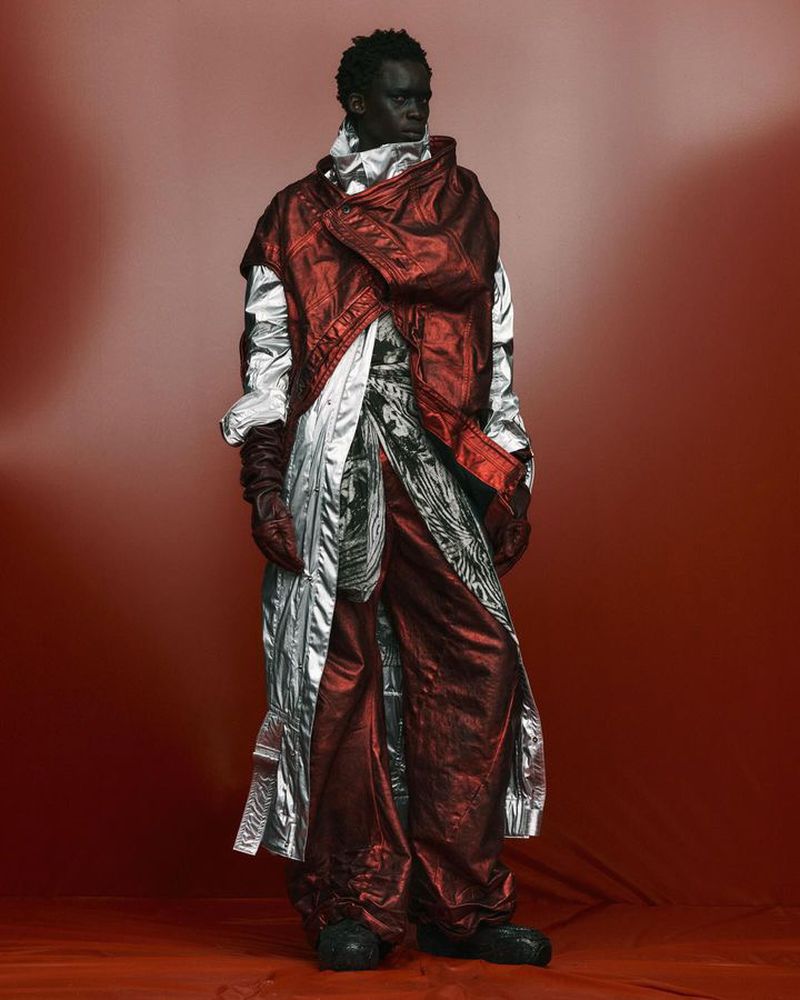 Full shot of a fashion model in an elaborate red and silver metallic outfit posing against a red gradient background, studio lighting.