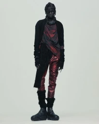 Model wearing a layered black cardigan, draped red top, metallic burgundy trousers, and chunky boots on a light seamless backdrop.