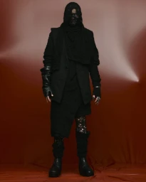 Model in layered black avant-garde streetwear featuring a hooded scarf and leather gloves against a rust backdrop