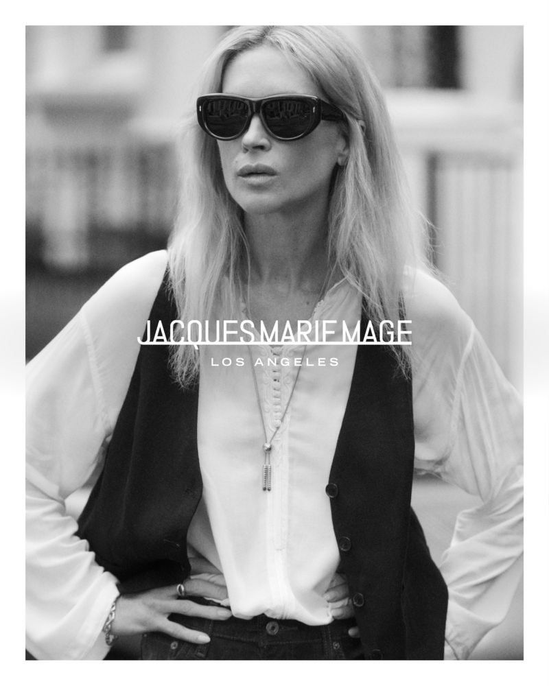 Model Erin Wasson wearing bold dark sunglasses, a white blouse, and a black waistcoat outdoors in black and white.