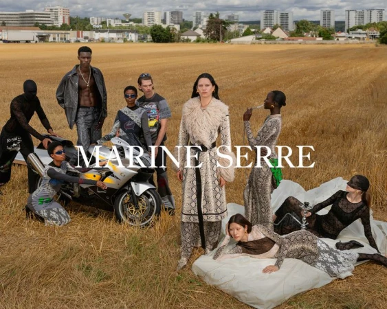 Editorial fashion shot with a diverse group of models in wheat field; cityscape visible in the background; MARINE SERRE logo overlay.