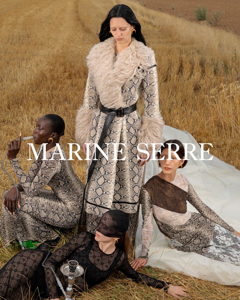 Fashion editorial showcasing four adult women in designer outfits in a golden field, with prominent brand logo text and hookah pipe.