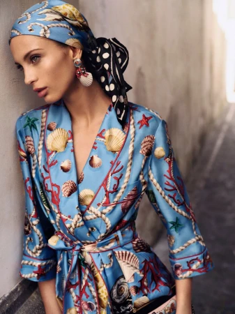 Woman in patterned scarf and robe poses indoors. She has earrings, light skin, and appears to be in her early adult years.