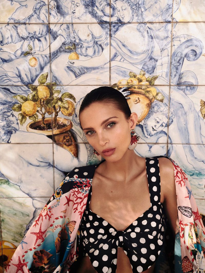 Elegant woman in a black and white polka dot crop top poses in front of a blue and white tiled wall with lemons and figures.