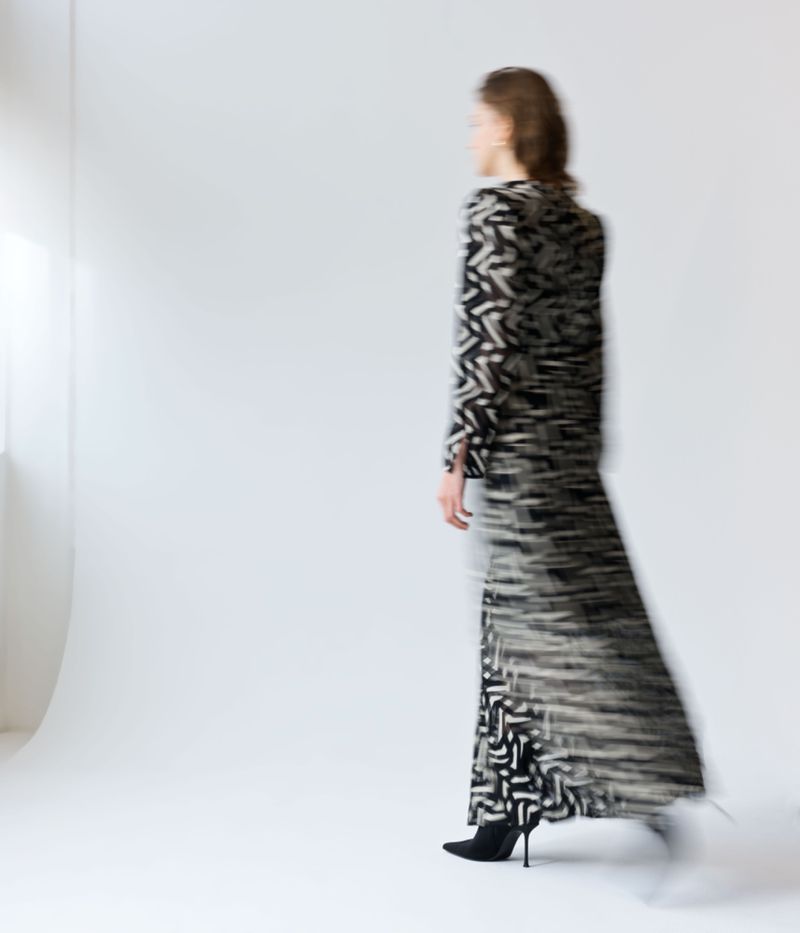 Blurred full-length shot of an adult woman in a patterned black-and-white dress with high-heeled shoes, motion-blurred in a photo studio.