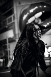 Model Kinari Tamukai with windblown dark hair wearing a black draped shirt on a Tokyo street for Yohji Yamamoto AW24.