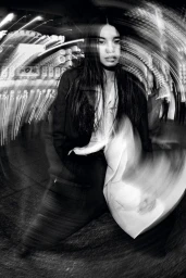 Kinari Tamukai wearing a black jacket and white shirt in a black and white dynamic rotational blur night shot.