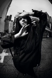 Model in black shirt posing with hands raised in Tokyo street captured in fisheye monochrome
