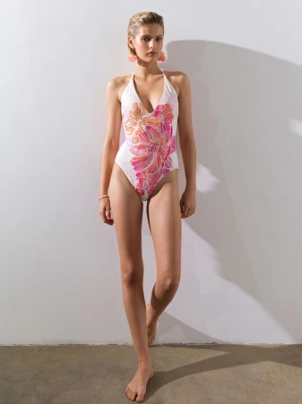 Model Aria Shine posing in a floral print halterneck one-piece swimsuit against a plain white studio wall.