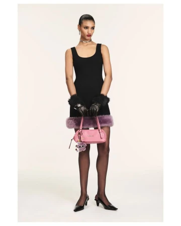 Full shot of a slender woman in a black dress, stockings, and heels, holding a pink purse with a furry charm, set against a plain backdrop.