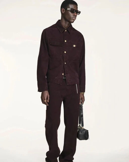A tall, dark-skinned man is showcased in a full-body shot, wearing a maroon corduroy jacket, matching pants, and black sunglasses against a white backdrop.