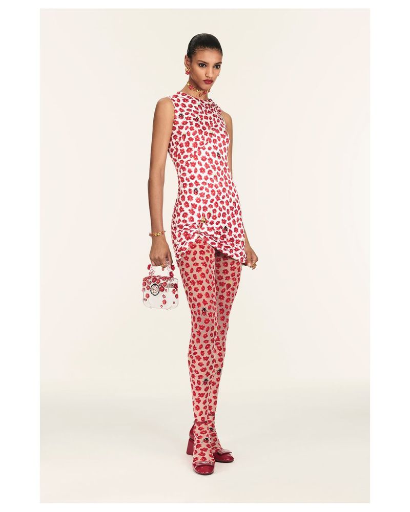 Fashion model wears a red and white dress and tights with a matching purse in a studio shot against a white backdrop.