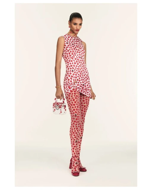 Fashion model wears a red and white dress and tights with a matching purse in a studio shot against a white backdrop. 