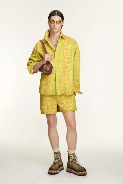 Male fashion model in patterned shirt and shorts with platform boots and shoulder bag posing in a full shot on a white background.