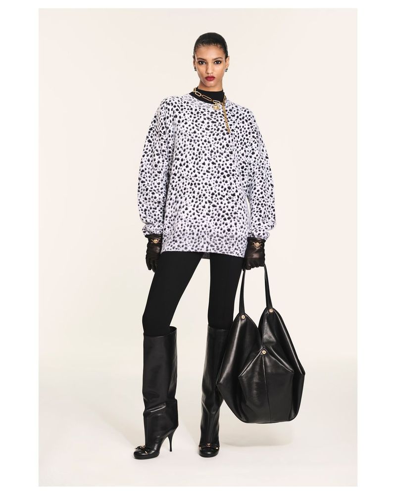 A woman models a Dalmatian-spotted sweatshirt with black leggings, high-heeled boots, a large black handbag, and gold chain necklace.