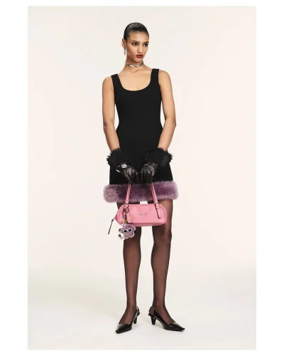 Model wearing a black sleeveless dress with purple faux fur trim holding a pink handbag against a neutral white background