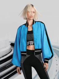 Patricia Zajac poses in an electric blue bomber jacket, black sports crop top, and geometric-patterned leggings.