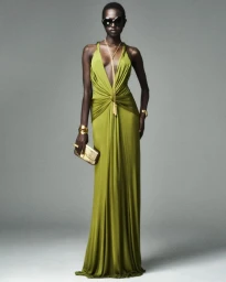 Model wearing a plunging chartreuse green draped maxi dress with dark oversized sunglasses and gold accessories on a grey backdrop.