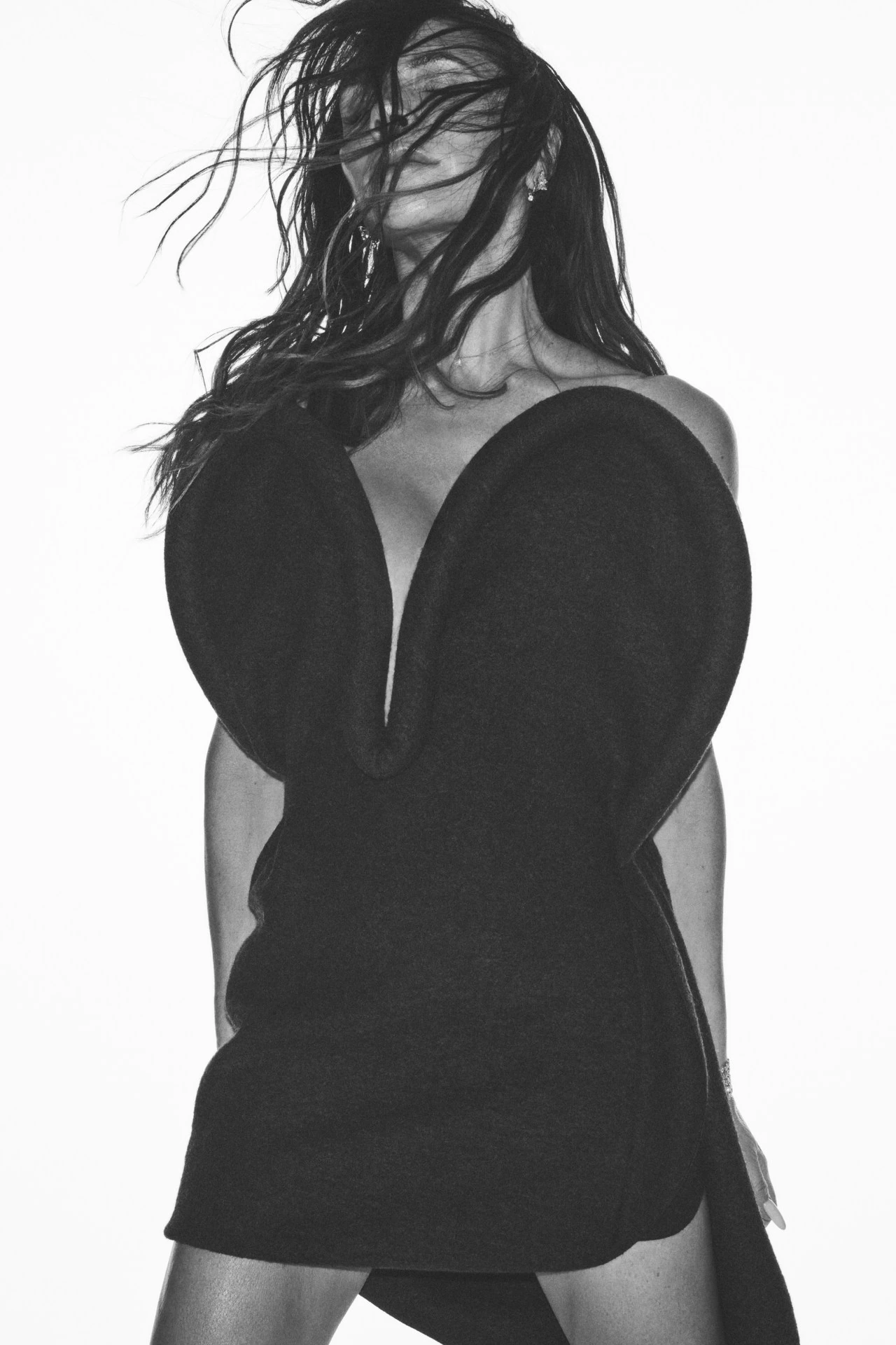 Monochrome studio shot of a woman with long dark hair wearing a black dress. The background is plain white creating a high-contrast image.
