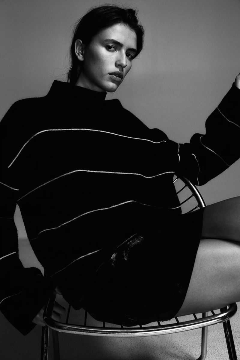 Model Adele Aldighieri seated on a metal chair wearing a dark striped turtleneck sweater for H&M