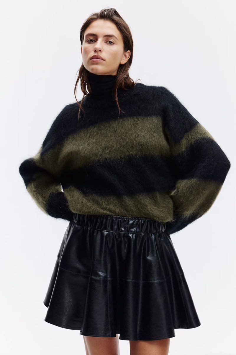 Fashion portrait of a woman wearing a black and olive green striped sweater and a black mini skirt in a bright photo studio.