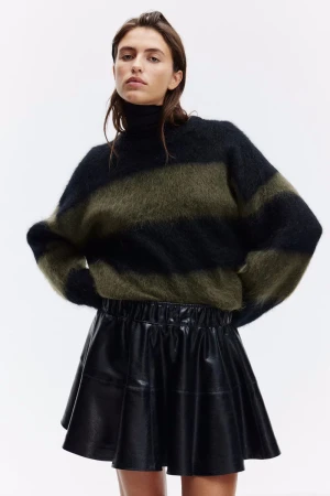 Fashion portrait of a woman wearing a black and olive green striped sweater and a black mini skirt in a bright photo studio.