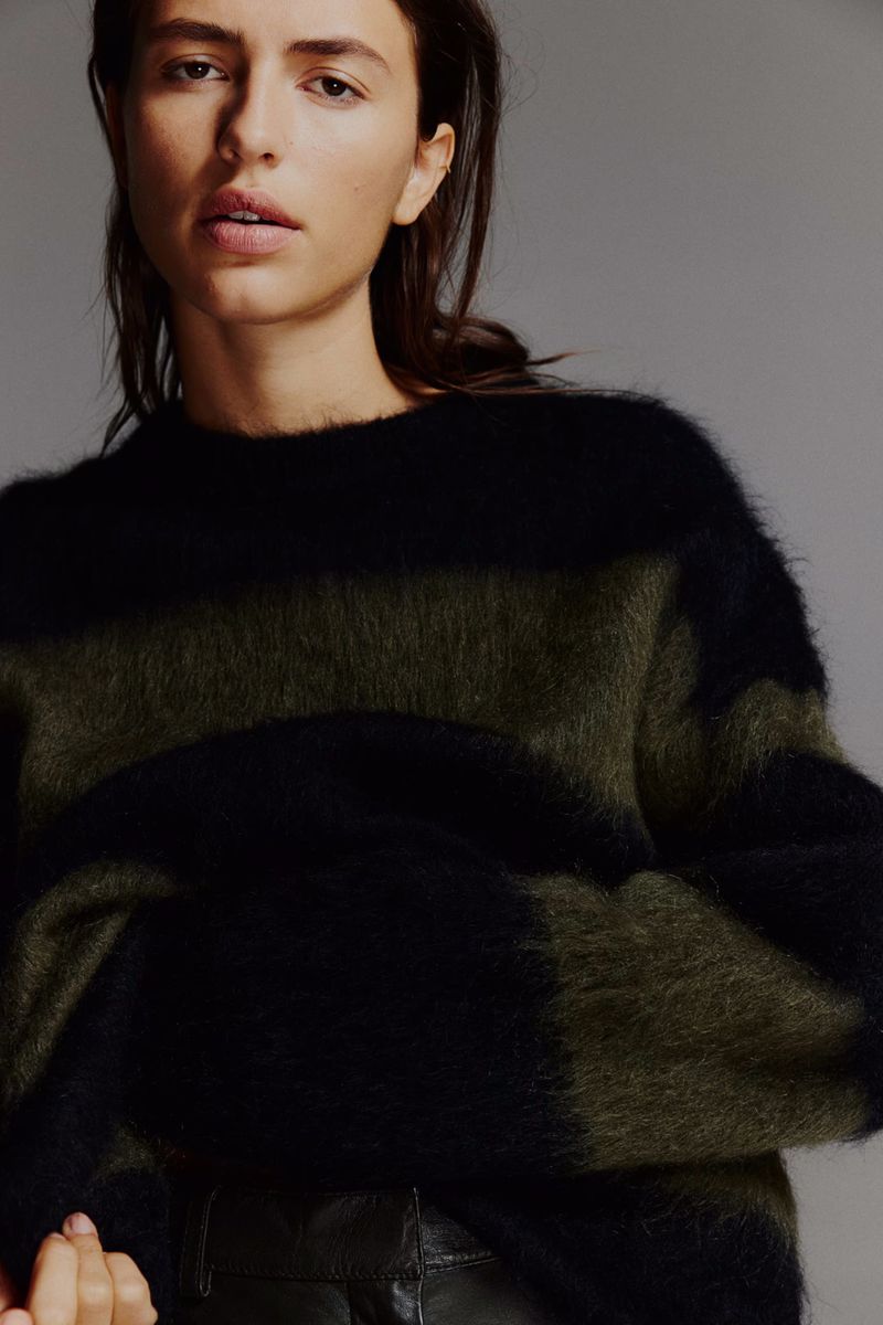 Portrait of a woman wearing a striped olive green and black sweater looking at the camera in a studio setting. Fashion shot.