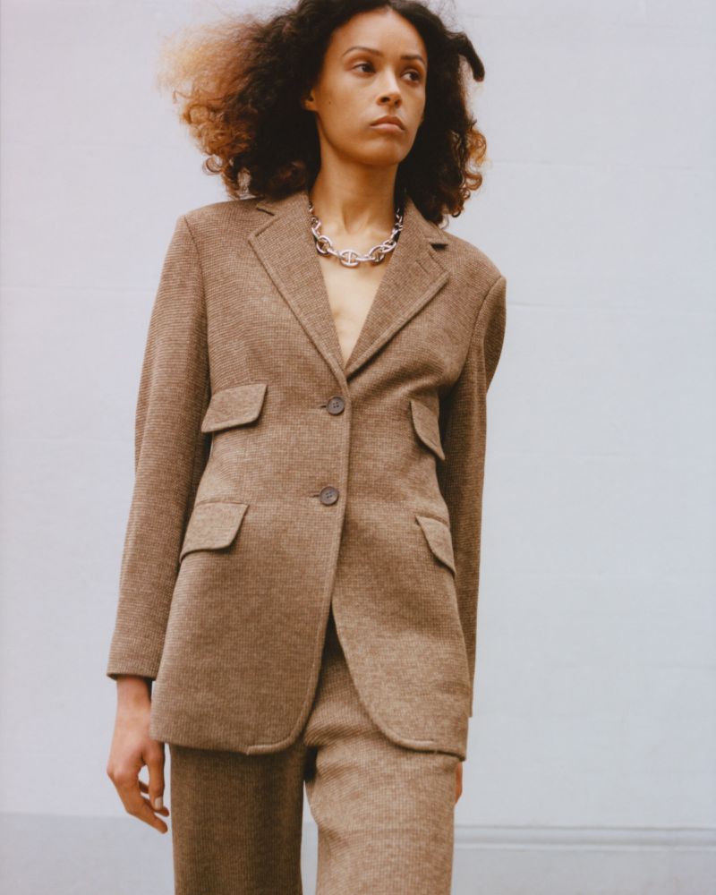 Model Prinnie Stott poses in a structured brown tailored blazer and silver chain necklace for Eudon Choi Resort 25.