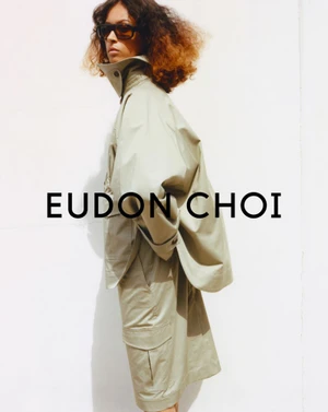 Model in dark sunglasses wearing a khaki coat and shorts against a white background for Eudon Choi Resort 25