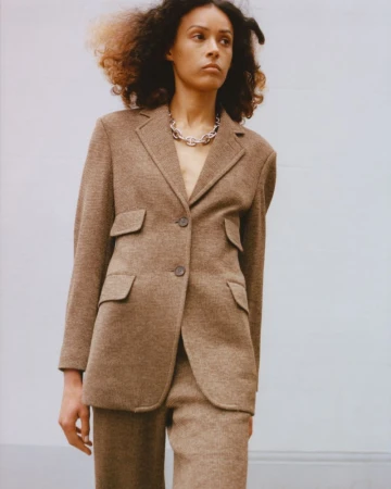 Model Prinnie Stott poses in a structured brown tailored blazer and silver chain necklace for Eudon Choi Resort 25.