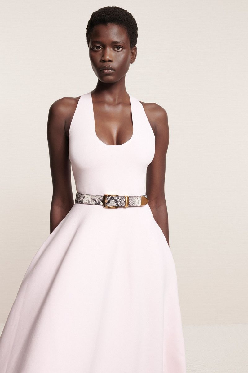 Portrait of a Black woman posing in a pale pink halter dress with a snakeskin belt, captured in a fashion forward, full studio shot.