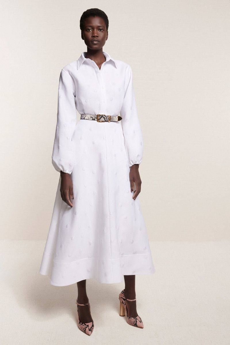 Full-length studio shot of an African woman in a white collared dress with a snakeskin belt and matching heels against a neutral backdrop.