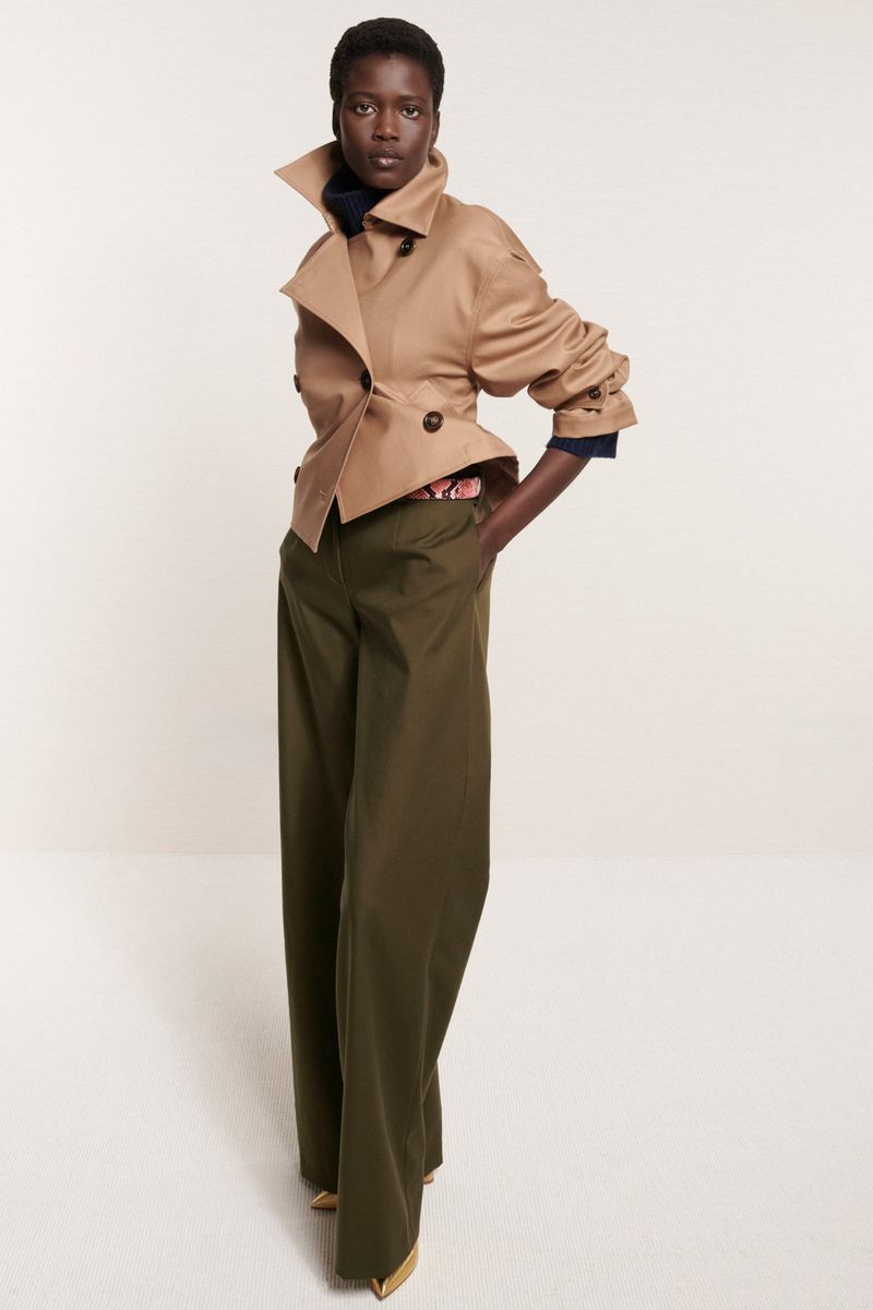 A woman models a tan cropped jacket with a wide collar and olive green wide-legged pants against a neutral background, showcasing modern fashion.