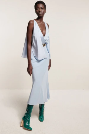 Model in pale blue silk dress and green boots posing against a neutral studio background