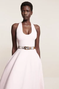 Model wearing a light pink halter dress with a patterned belt against a seamless backdrop