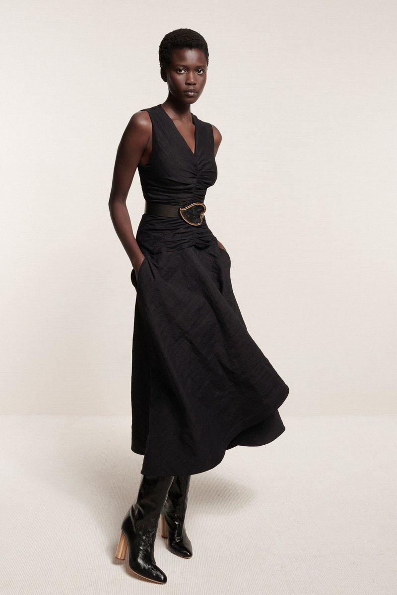 Model in black V-neck dress and boots standing against a neutral background for Brandon Maxwell Resort 2025 Lookbook
