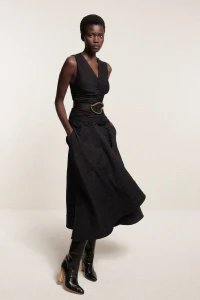 Model in black V-neck dress and boots standing against a neutral background for Brandon Maxwell Resort 2025 Lookbook