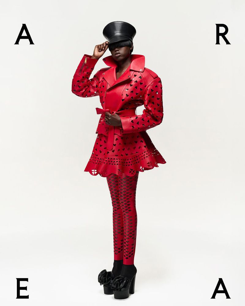 Fashion model poses in a red coat and leggings with black heart details against a white background with the letters A, R, and E.