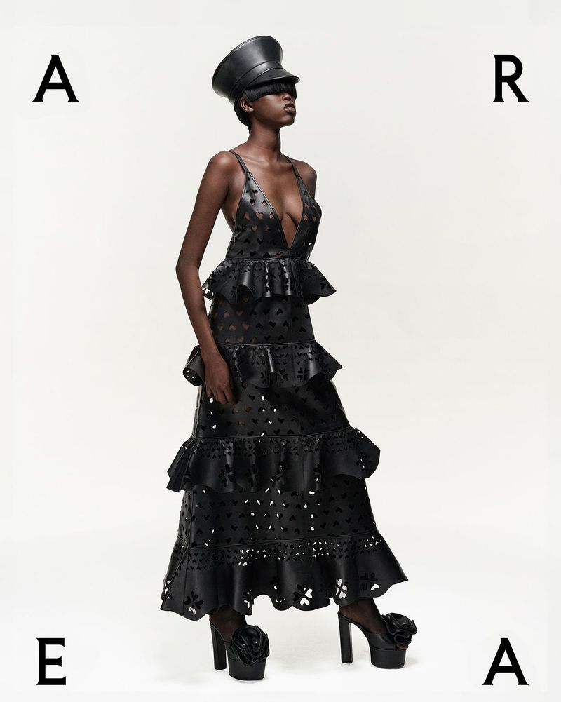 Fashion editorial shot of a Black model in a black leather dress and hat against a white background, styled as an Ace card.
