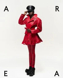 Model in red cutout jacket and matching patterned tights wearing a black cap against a plain white background