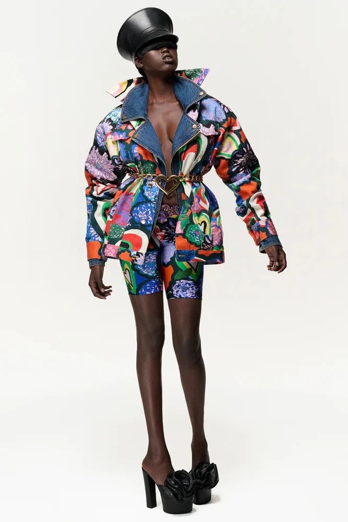 Model in printed colourful patterned jacket and matching shorts wearing black high heels against a white background