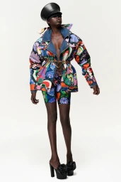 Model in printed colourful patterned jacket and matching shorts wearing black high heels against a white background