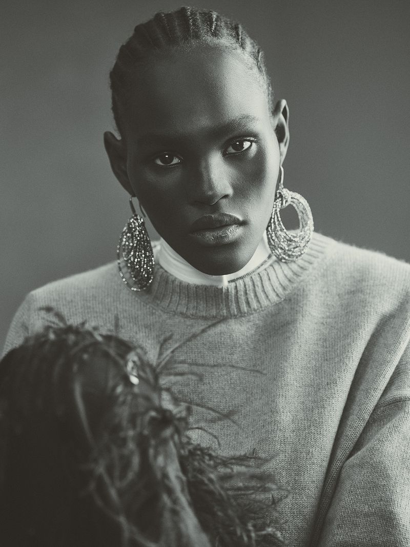Close-up portrait of a Black woman with braided hair wearing a light sweater and statement earrings in a studio setting.